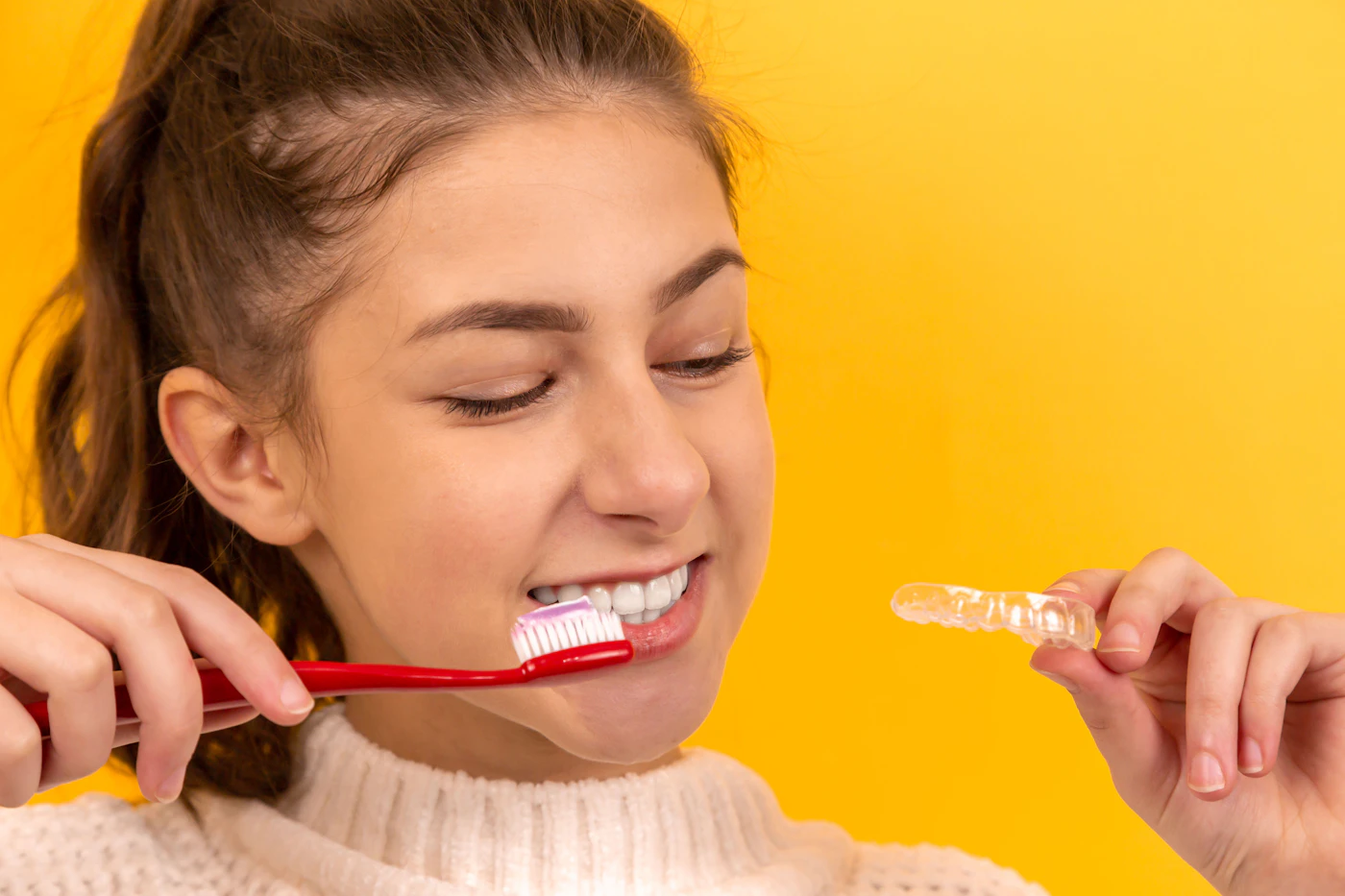 A smiling girl holding a toothbrush and a clear retainer
